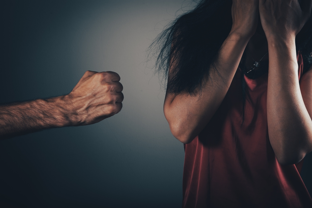 A raised fist threatens a woman covering her face with her hands
