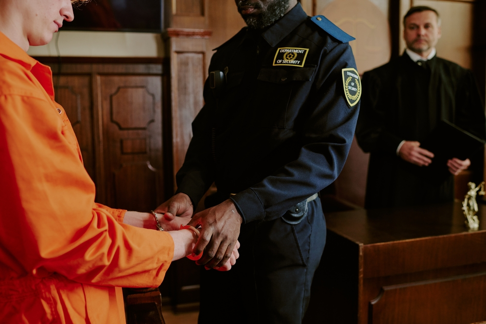 Defendant in handcuffs escorted by a security officer in a courtroom.