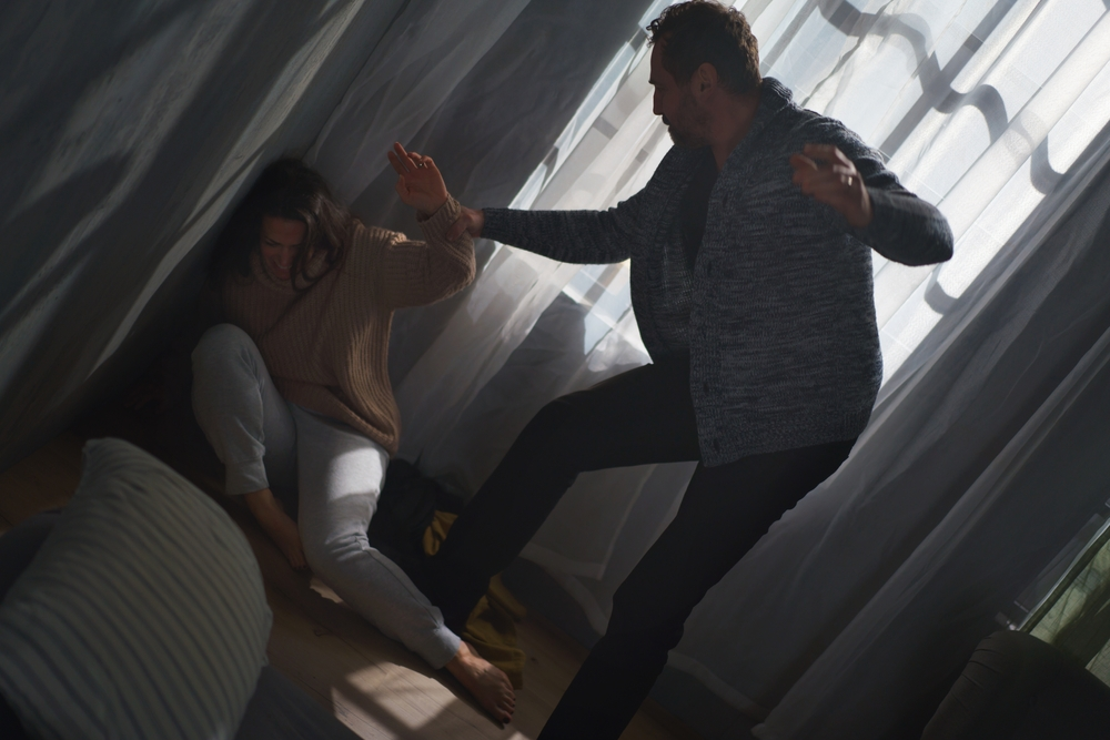 Man raising his hand while a woman crouches on the floor in fear during a tense domestic dispute inside a home.